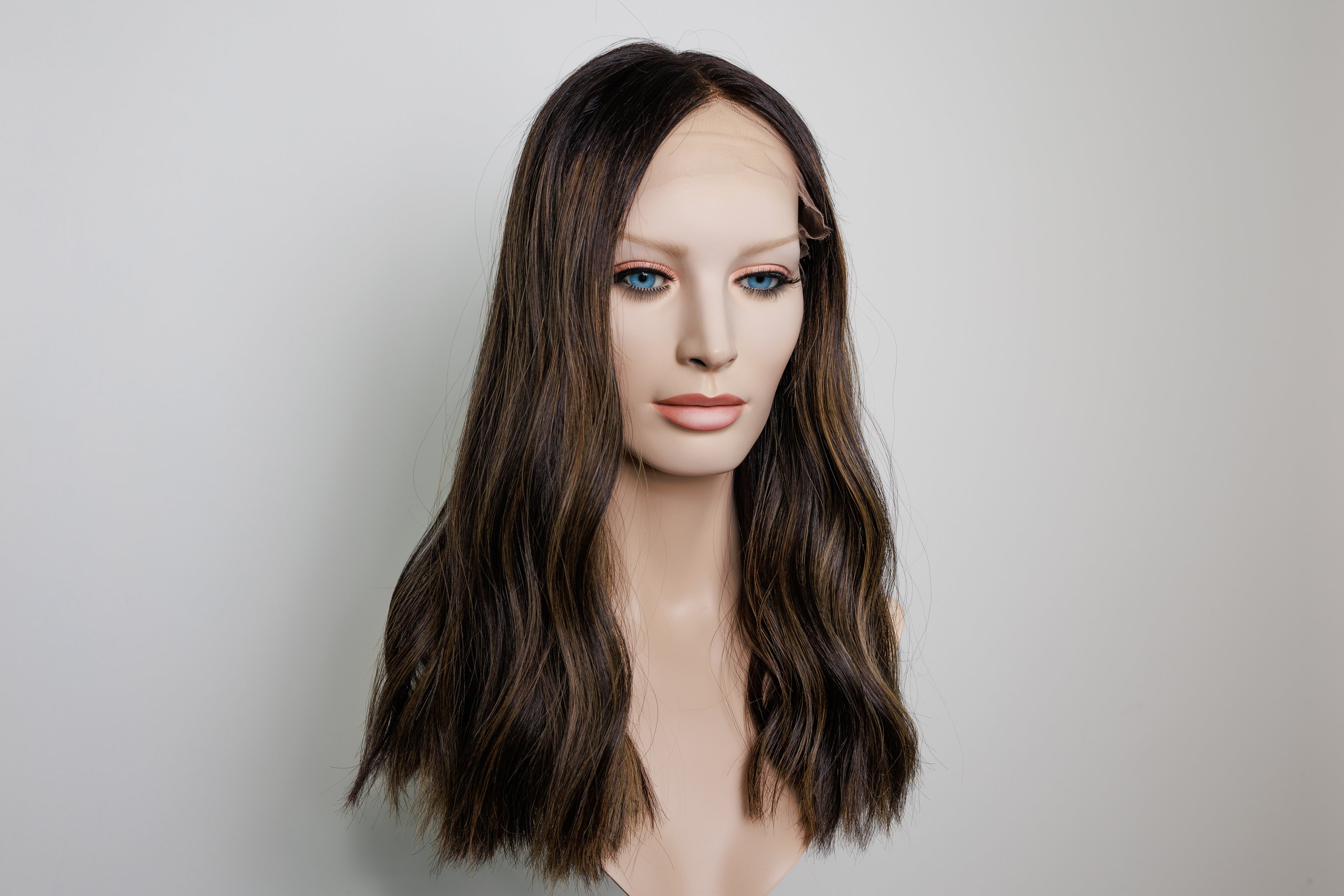 A shoulder-length wavy wig with dark brown roots and lighter caramel-brown highlights, displayed on a mannequin head against a plain light gray background.